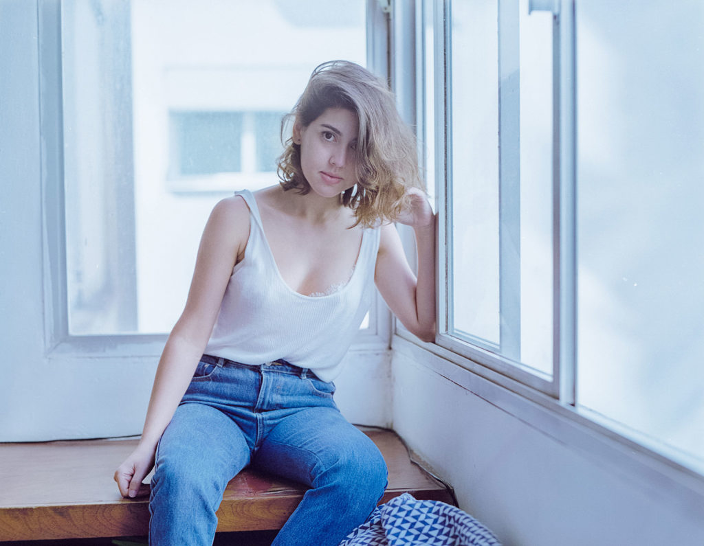 Modelo de calça jeans azul sentada na janela, fotografia analógica