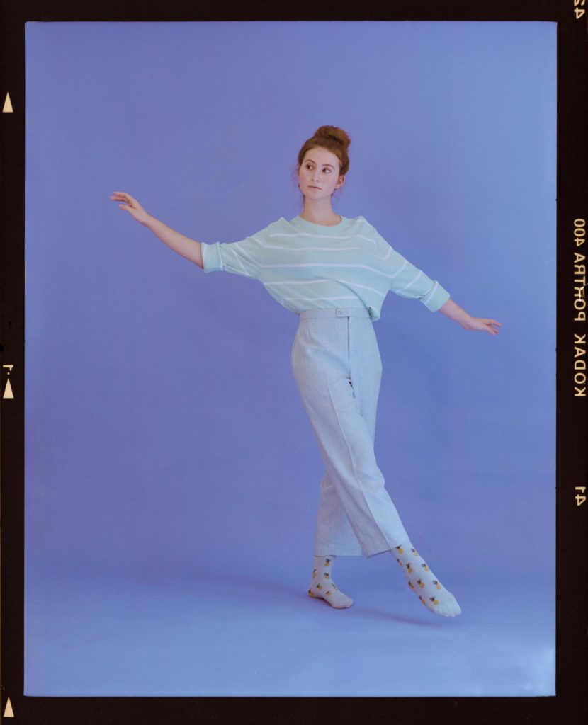 Foto de filme de médio formato com bordas do negativo - Modelo em pose de bailarina no estúdio com fundo azul e tons pasteis - porque fotografar com câmeras analógicas