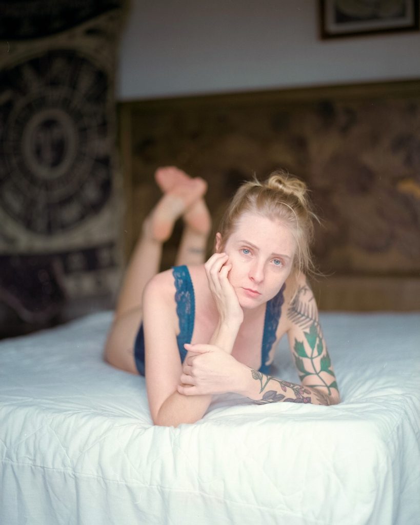 Como fotografar com luz difusa, exemplo de retrato de garota loira com maiô azul deitada em uma cama com lençóis brancos