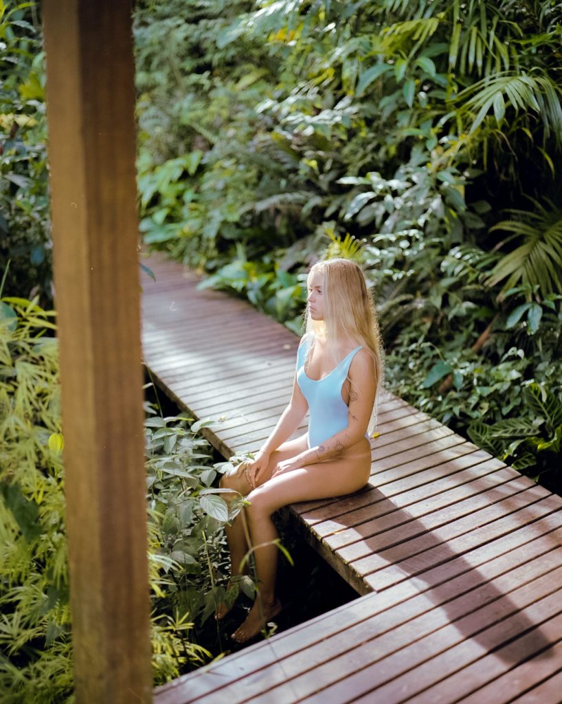 Garota loira sentada em deck de madeira sob luz dura em contraluz